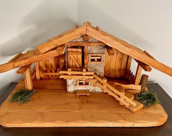 May include: A wooden miniature cabin with a sloped roof, small windows, and a wooden door. The cabin is constructed from various sizes of wood pieces and sits on a wooden base. Green moss accents the base.