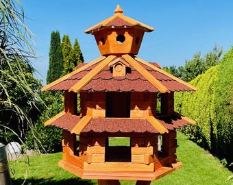 Könnte beinhalten: Ein Vogelhaus aus Holz mit mehrstöckigem Design und einem roten Schindeldach. Das Haus ist auf einem hohen Holzpfahl montiert.