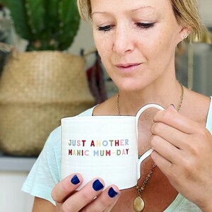 May include: White ceramic mug with a colorful text design that reads "Just Another Manic Mum-Day".