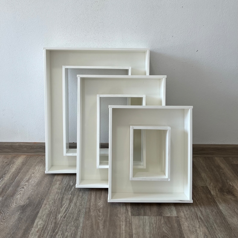 May include: Four white square picture frames, nested inside each other, with the largest frame at the bottom and the smallest frame at the top.