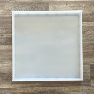 Op de afbeelding: Een witte vierkante siliconen mal met een glad oppervlak. De mal ligt op een houten achtergrond.