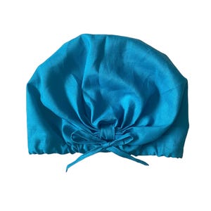 May include: A turquoise blue fabric shower cap with a gathered top and a tie closure.