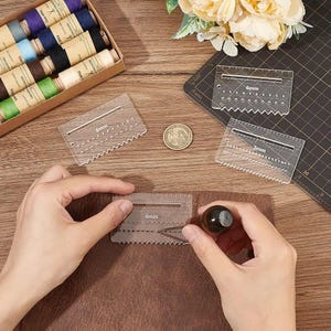 May include: A craftsperson uses a 4mm leather hole spacing tool on brown leather. Other tools include 3mm and 6mm spacing tools, a box of thread spools, and a cutting mat. A coin is also visible.