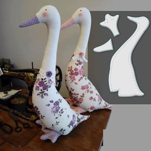 May include: Two handmade goose plushies with white bodies, long necks, and patterned wings. One goose has purple floral fabric, the other pink. Both have dotted beaks and decorative neck accents. A pattern is shown on the right.