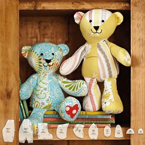 May include: Two patchwork teddy bears, one blue and green, the other yellow and pink, sitting on a shelf with a stack of books and fabric pattern pieces.