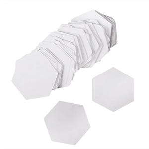 Puede incluir: Una pila de baldosas hexagonales blancas, con tres baldosas separadas de la pila principal. Las baldosas son de color blanco brillante y parecen estar hechas de papel o un material similar. La imagen está tomada desde un ángulo alto.