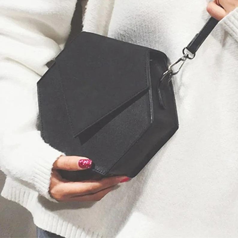May include: A black geometric shaped crossbody bag with a long strap. The bag has a unique, modern design.