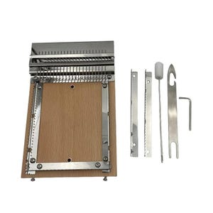 Puede incluir: Un telar de tejido de madera con un marco de metal y un juego de herramientas de metal. El telar tiene una base rectangular de madera con un marco de metal y una serie de dientes de metal. Las herramientas incluyen una aguja, un gancho y una llave pequeña.