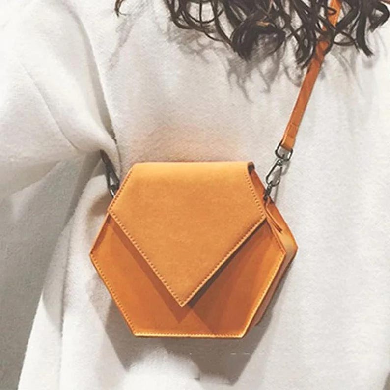 May include: A small, orange, hexagonal-shaped crossbody bag with a flap closure and a chain strap.