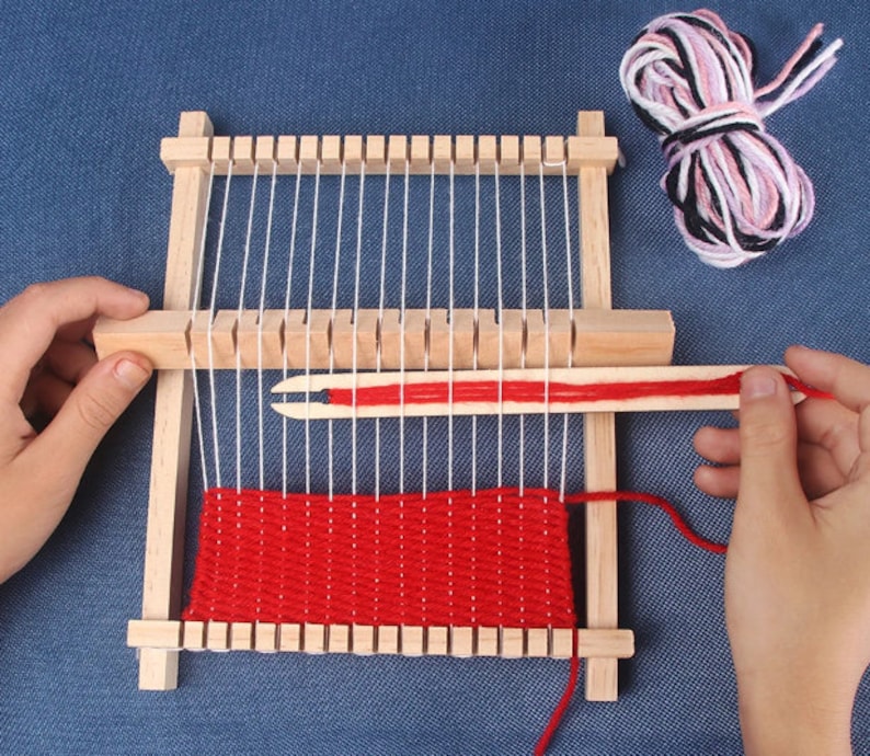 May include: A wooden loom with red yarn woven into a red and white pattern. The loom has a wooden shuttle and a wooden needle.