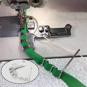 May include: A sewing machine foot attachment for creating a rolled hem. The foot is made of metal and has a green fabric guide. The foot is attached to a sewing machine and is being used to sew a green fabric strip.