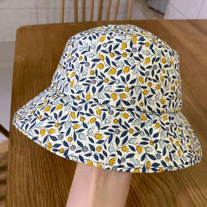 Peut inclure: Un chapeau bob blanc avec un motif floral bleu et jaune. Le chapeau a une large bordure et une couronne plate.