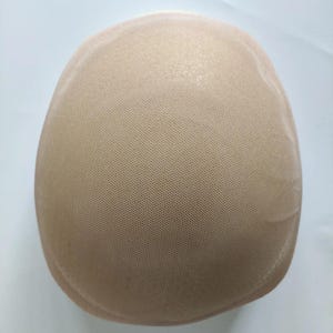 May include: A beige, dome-shaped wig cap made of a fine, mesh-like material. The cap is designed to fit the head and is likely used as a base for wigs or hairpieces. The color is a neutral tone, suitable for various skin tones.