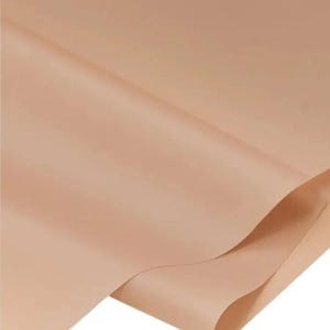 May include: A close-up of a sheet of light brown paper with a smooth, matte finish. The paper is slightly folded, creating soft shadows and highlighting the texture. The color is a warm, neutral tone.