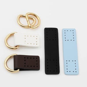 Puede incluir: Un surtido de suministros de artesanía en cuero, que incluye anillas en D doradas, piezas de cuero blancas, marrones, negras y azul claro con agujeros pretaladrados para coser. Ideal para la fabricación de bolsos y proyectos de cuero.