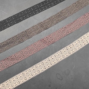 May include: Four strips of decorative lace trim arranged diagonally. The colours include black, dark grey, dusty rose, and cream. Each strip features a consistent openwork pattern with scalloped edges, showcasing a delicate, woven texture throughout.