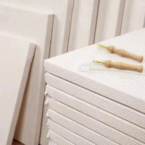 May include: A stack of white canvas boards with two wooden needle tools for embroidery or cross stitch.