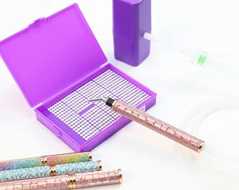 Puede incluir: Un conjunto de herramientas para nail art, que incluye un bolígrafo rosa con textura de cocodrilo, un recipiente morado con cuentas blancas y varios bolígrafos con texturas brillantes y de cocodrilo. Para nail art.