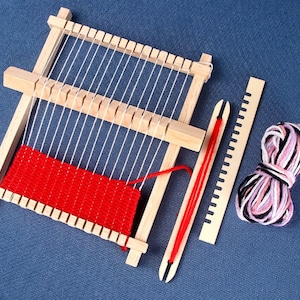 May include: A wooden loom with red yarn woven into the frame. A wooden needle and a ball of pink and black yarn are also included.