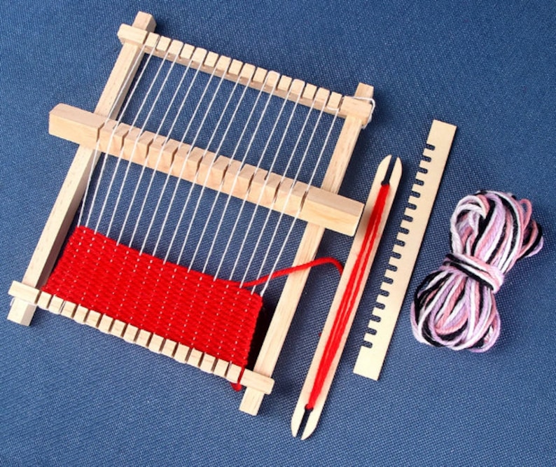 May include: A wooden loom with red yarn woven into the frame. A wooden needle and a ball of pink and black yarn are also included.