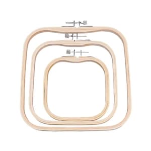 May include: Three nested square embroidery hoops made of light-colored wood. Each hoop features a metal tension screw mechanism at the top center for adjusting the tightness of the frame. The hoops are arranged from largest to smallest.
