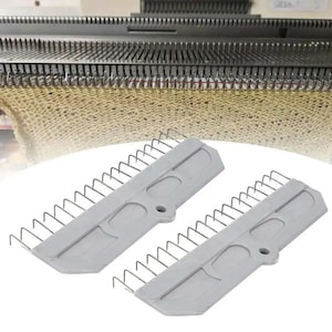 May include: Two grey knitting machine transfer tools with metal hooks are in the foreground. The background shows a knitting machine with many metal needles and a knitted fabric in progress. The tools are used to transfer stitches.