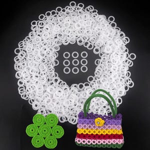 May include: A collection of white rubber rings, a small crocheted purse with a green handle, and several green crocheted circles are displayed against a black background. The purse is multi-colored with a yellow flower accent.