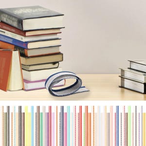May include: A collection of books with different coloured covers, and a blue and white ribbon. A selection of colourful ribbons are displayed at the bottom of the image. The books are on a light wooden surface.