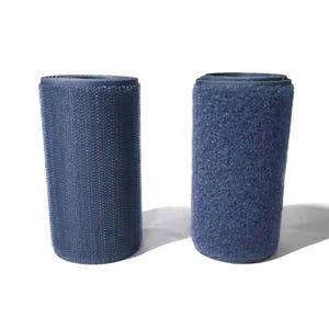 Può includere: Due rotoli di materiale di fissaggio a strappo blu. Uno ha una superficie strutturata, l'altro una superficie ad anello. I rotoli cilindrici sono in piedi su uno sfondo bianco.