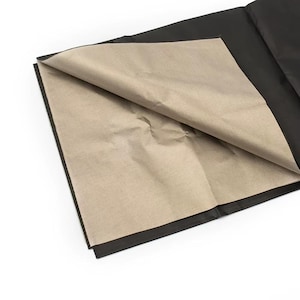 May include: A close-up shot of a black sheet of paper with a tan sheet of paper folded over it. The tan paper is crumpled, and the black paper is smooth. The edges of the black paper are visible.