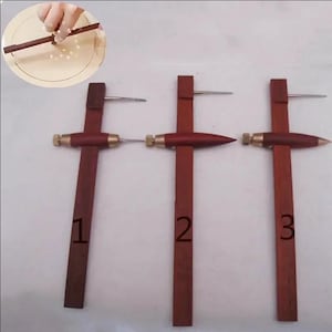 May include: Three wooden compasses with metal tips and brass accents. The compasses are numbered 1, 2, and 3. The wood is a dark reddish-brown color. One compass is being used to draw a circle.