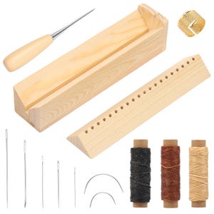 Puede incluir: Un conjunto de herramientas y suministros para artesanía en cuero, que incluye un potro de costura de madera, agujas, carretes de hilo, una lezna y un dedal dorado. Las herramientas de madera son de color claro.