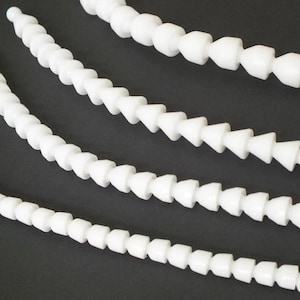 Könnte beinhalten: Nahaufnahme von mehreren weißen, flexiblen, segmentierten Schläuchen. Jedes Segment hat eine konische Form, die Ende-an-Ende verbunden ist und ein kettenartiges Aussehen erzeugt. Die Schläuche sind in gebogenen Linien vor einem dunklen Hintergrund angeordnet.