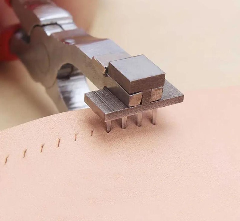 May include: A close-up of a leather sewing tool with a metal base and a set of prongs. The tool is being used to punch holes in a piece of leather.