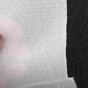 May include: Close-up of a white, semi-transparent fabric with a grid-like pattern. The fabric is positioned against a black background, creating a contrast. The texture appears delicate and lightweight, suggesting a potential use in apparel or crafts.