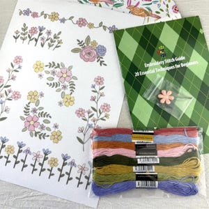 May include: An embroidery kit with floral patterns and a stitch guide. The kit includes a selection of colourful embroidery floss, a flower-shaped pin, and a booklet titled "Embroidery Stitch Guide: 20 Essential Techniques for Beginners."