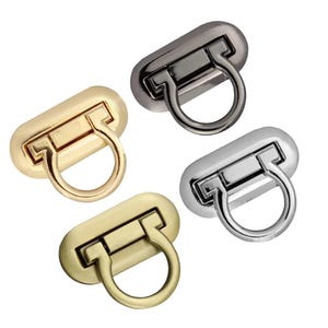 May include: Four metal purse clasps in gold, gunmetal, silver, and antique brass finishes. Each clasp has an oval base with a rectangular bar and a circular ring. The clasps are arranged diagonally against a white background.