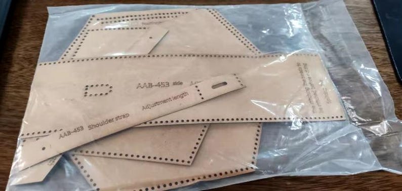 May include: A set of leather patterns for a bag or purse project. The patterns are labeled "AAB-453 side" and "AAB-453 shoulder strap" and include an adjustment length piece.
