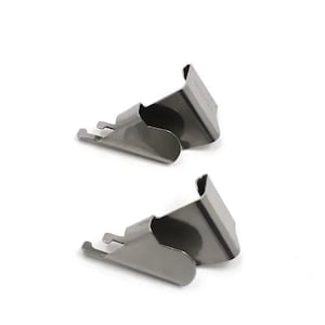 Könnte beinhalten: Zwei silberfarbene Metallclips mit geschwungenem Design. Jeder Clip hat eine kleine, rechteckige Lasche, die sich von der Basis erstreckt, und eine gebogene Oberseite. Die Clips sind vor einem weißen Hintergrund platziert.