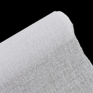 Pode incluir: Um pedaço enrolado de tecido de gaze branco contra um fundo preto. O tecido tem uma trama fina e aberta, com as bordas ligeiramente desfiadas. A textura da gaze é visível, com uma aparência ligeiramente translúcida.