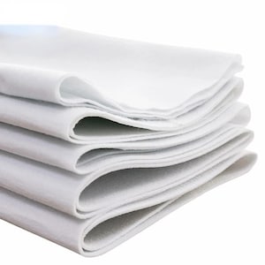 May include: A stack of folded white fabric sheets with a soft, matte texture. The layers are neatly piled, showing the thickness and consistent white color of the material. The edges are smooth and clean, creating a layered appearance.
