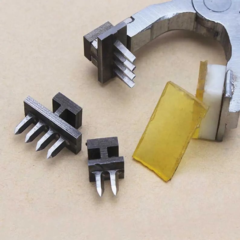 May include: Four metal tools with sharp points, used for making holes in materials. The tools are arranged on a brown surface. A pair of pliers with a yellow rubber pad is also visible.