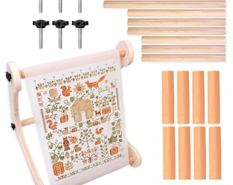 May include: A wooden embroidery hoop with a completed cross-stitch design featuring a house, pumpkins, and a fox. Includes wooden dowels, tension knobs, and fabric strips. The cross-stitch design is in shades of orange, green, and brown.