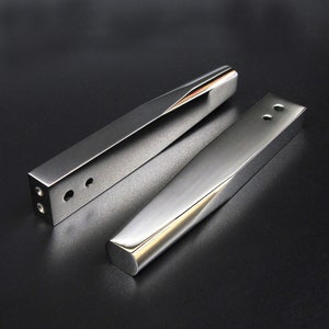 Può includere: Due maniglie per porte in metallo argentato con un design moderno. Le maniglie hanno una forma rettangolare con bordi arrotondati e una leggera curva al centro. Le maniglie hanno piccoli fori sul lato per il montaggio.