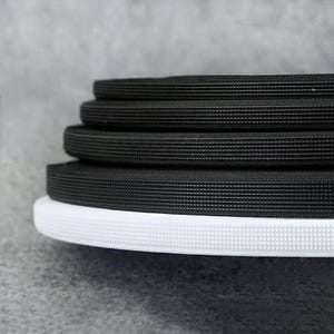 Könnte beinhalten: Nahaufnahme von schwarzem elastischem Besatz mit einer strukturierten Oberfläche. Der Besatz ist in einem Stapel gefaltet, mit einem weißen elastischen Besatz am Boden.