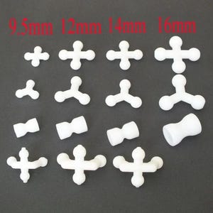 Puede incluir: Separadores de baldosas de plástico blanco en varios tamaños, incluyendo 9,5 mm, 12 mm, 14 mm y 16 mm. Los separadores tienen forma de cruz y de T, y formas cilíndricas. La imagen está sobre un fondo gris oscuro.