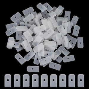 May include: A collection of small, translucent plastic rectangular pieces with a single hole in the center. The pieces are scattered across a black surface, with a row of similar pieces lined up at the bottom.