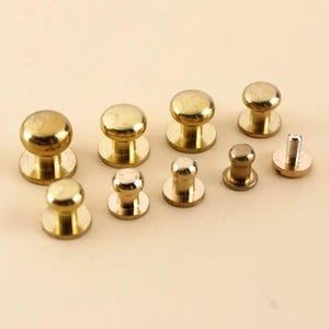 May include: A collection of brass-colored rivets and fasteners. The assortment includes various sizes of domed rivets and a screw-post rivet, all with a shiny, metallic finish. These hardware pieces are likely for leathercraft or similar projects.