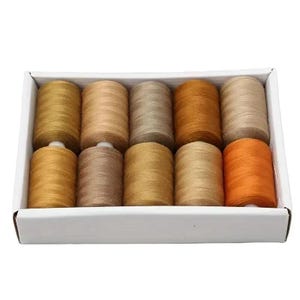 May include: A white cardboard box containing ten cylindrical spools of sewing thread arranged in two rows. The thread colours include various shades of tan, beige, gold, brown, and orange, all featuring a smooth, wound texture on each spool.