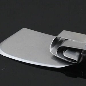 K&ouml;nnte beinhalten: Ein Teigschaber aus Edelstahl mit gebogener Klinge. Die Klinge ist rechteckig mit abgerundeter Kante. Der Griff besteht aus gefaltetem Metall. Das Werkzeug ist zum Backen und Kochen.